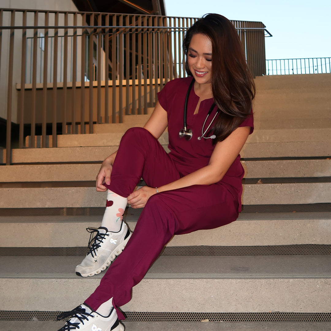 Person wearing maroon pants and white sneakers against a building exterior.