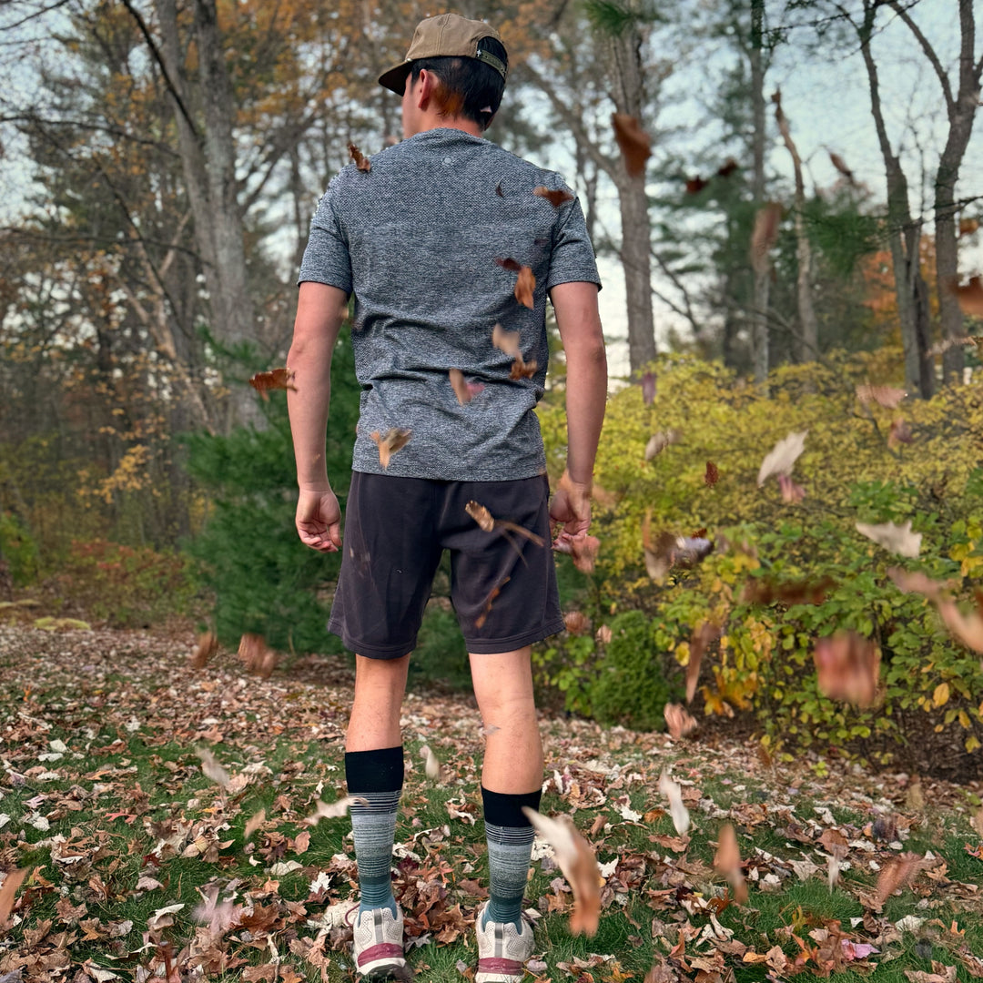 Person walking through a forest with fallen leaves on the ground