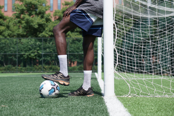 Person preparing to kick a soccer ball near a goalpost on a grass field performance socks compression