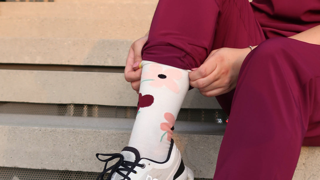 Person wearing white athletic shoes with black laces and maroon pants, sitting on a bench. lightweight compression socks