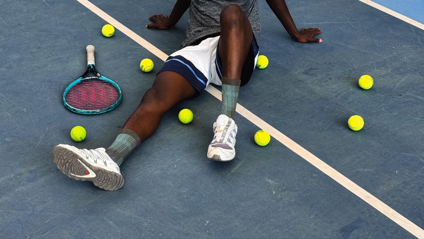 Person sitting on a tennis court with tennis balls and racket